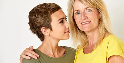 A mum embraces her teenage daughter with cancer