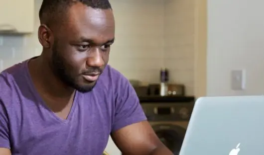 A young man with cancer sits in front of his laptop