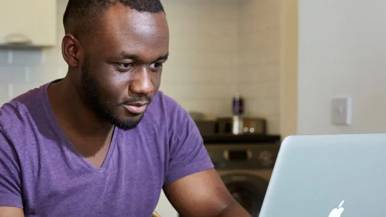 A young man with cancer sits in front of his laptop