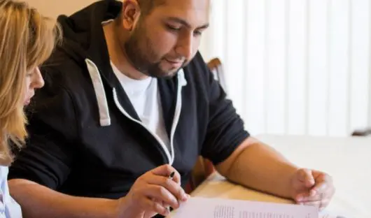 A young man with cancer sits at a table with a document