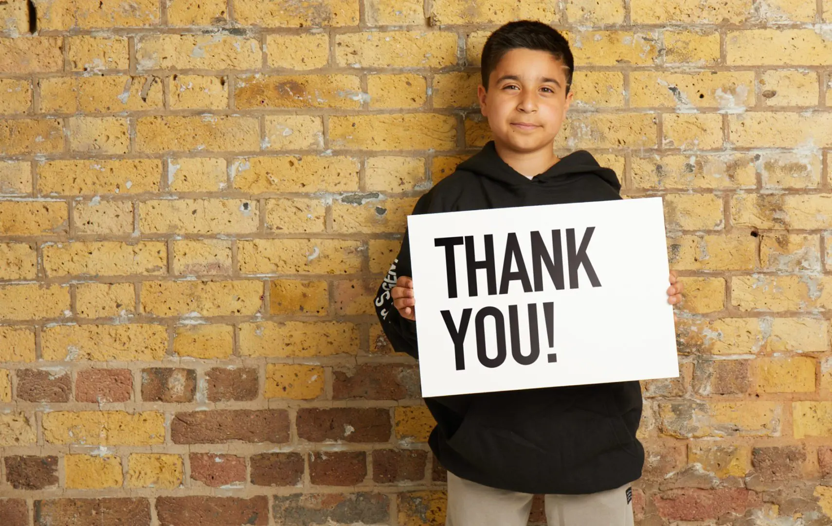 Sofyan, a young person we helped. holding a sign saying 'thank you'.