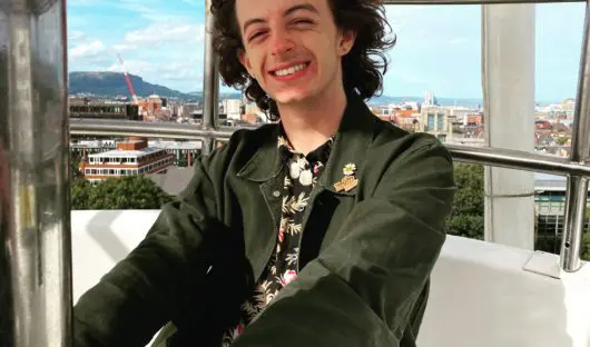 Conor smiling. He is sitting by a window on a sunny day.