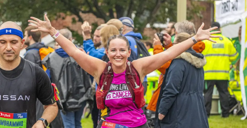 Runner with a Young Lives vs Cancer vest running to raise money for the charity. They are smiling with their arms up. 