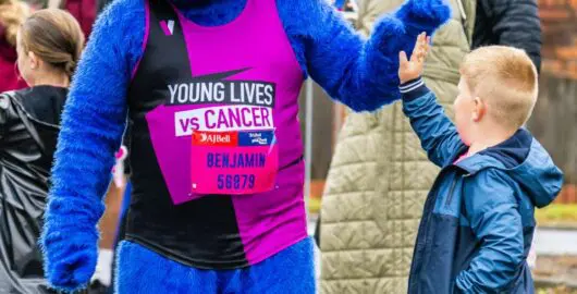 Runner dressed in a furry blue costume, high-fives a young man