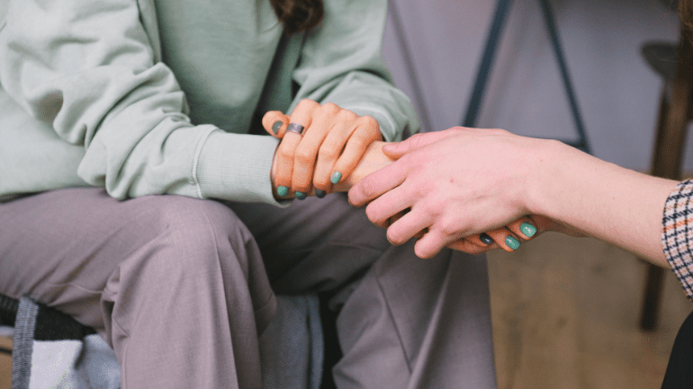 Someone holding another person's hand. One of the people has green painted nails.