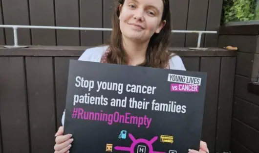 Young Lives vs Cancer Campaigns Manager holding sign reading Stop young cancer patients and their families running on empty