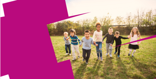 Web banner. image shows a group of 7 children all holding hands in a line, running towards the camera, smiling and looking excited