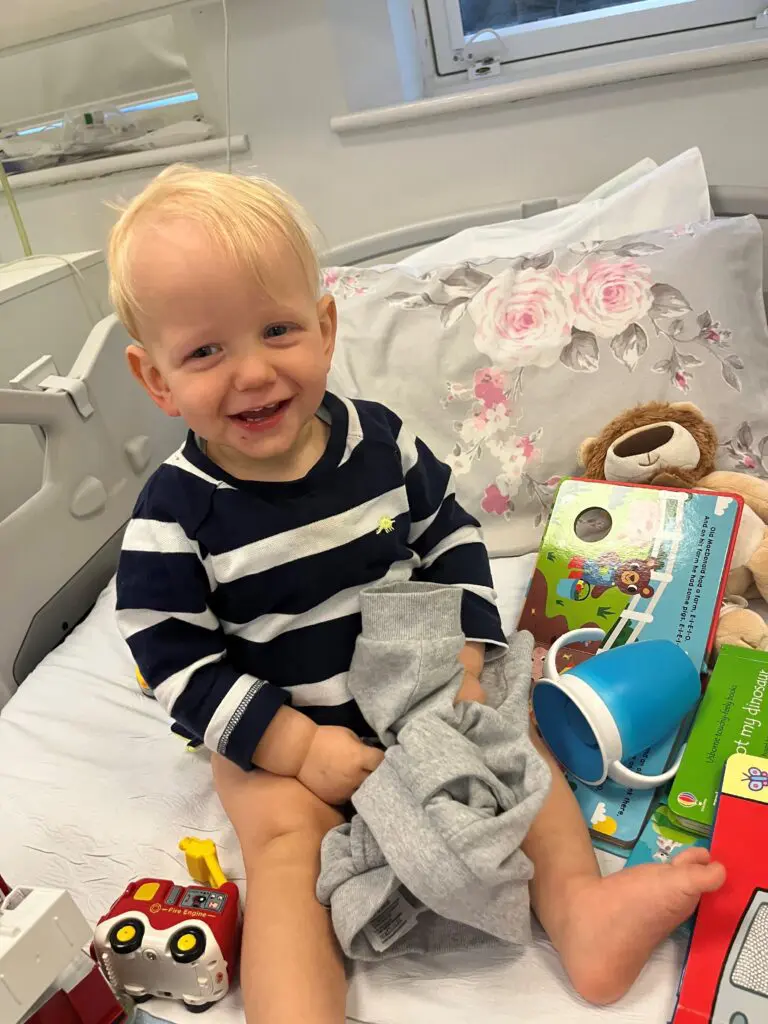 Young cancer patient Thomas sits smiling on a hospital bed with toys