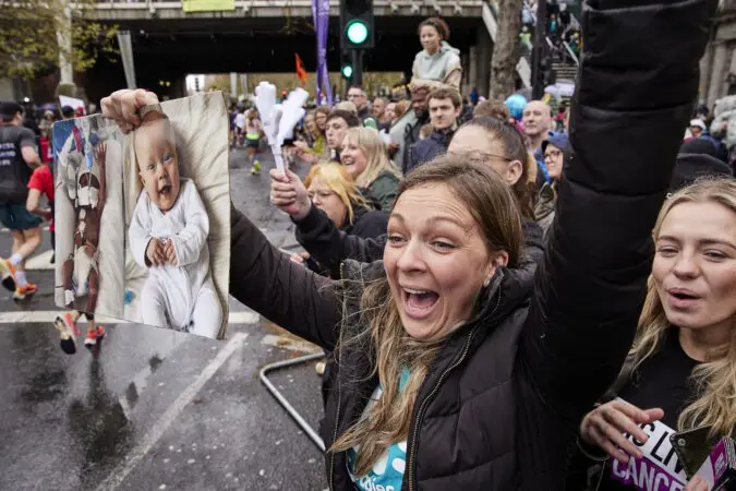 Woman with picture of a baby cheers on Young Lives vs Cancer London Marathon runners in the crowd