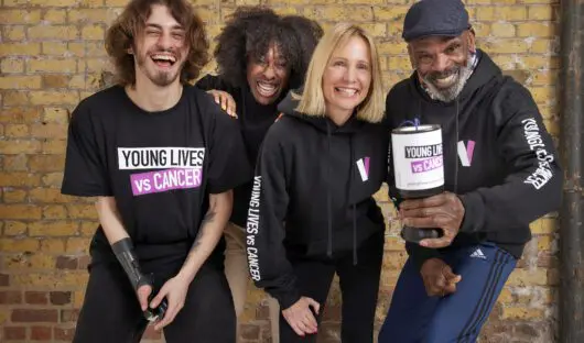 Four people stand together dressed in Young Lives vs Cancer clothing and one holds a collection pot.