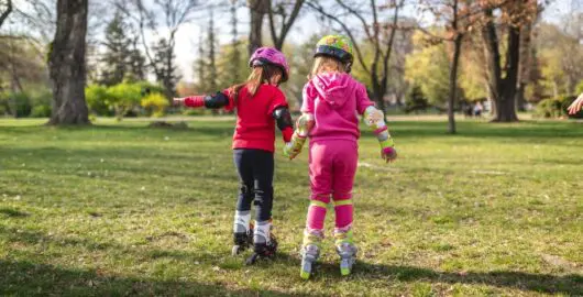 Two young children in the park on roller skates. Seen from the back