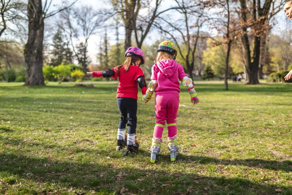 Two young children in the park on roller skates. Seen from the back