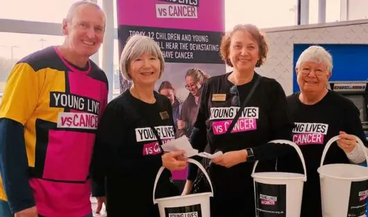 Four people with Young Lives vs Cancer T-shirts and collection buckets, smiling