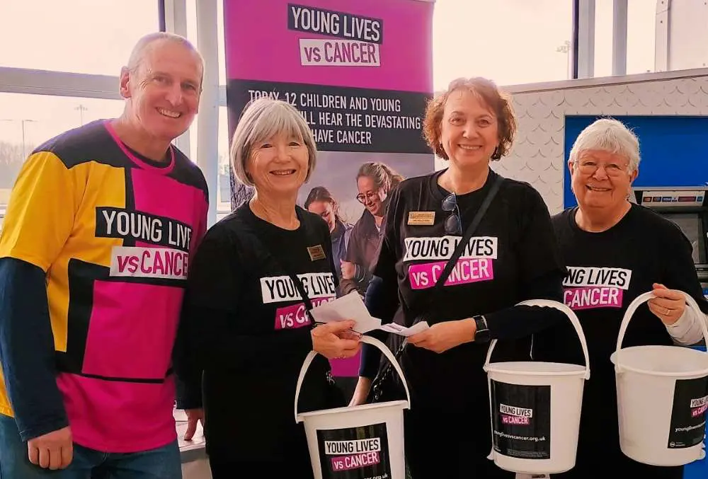 Four people with Young Lives vs Cancer T-shirts and collection buckets, smiling