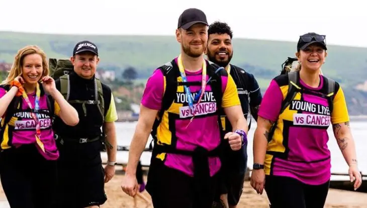 Group of people wearing Young Lives vs Cancer vests, walking by the sea on a grey day