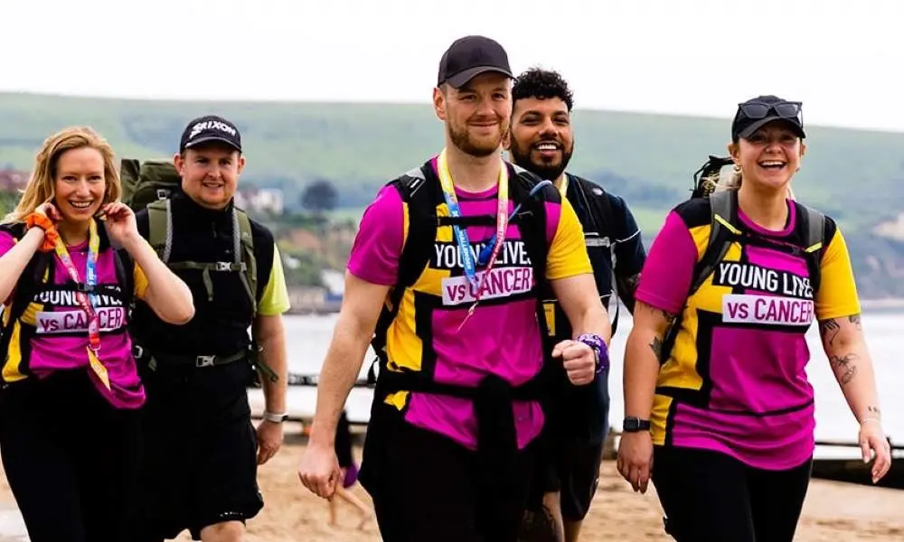 Group of people wearing Young Lives vs Cancer vests, walking by the sea on a grey day