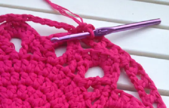 Close up of a crochet needle and pink wool made into a circle