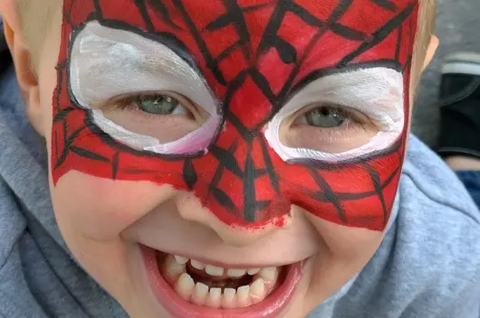 child smiling with face painted like spiderman
