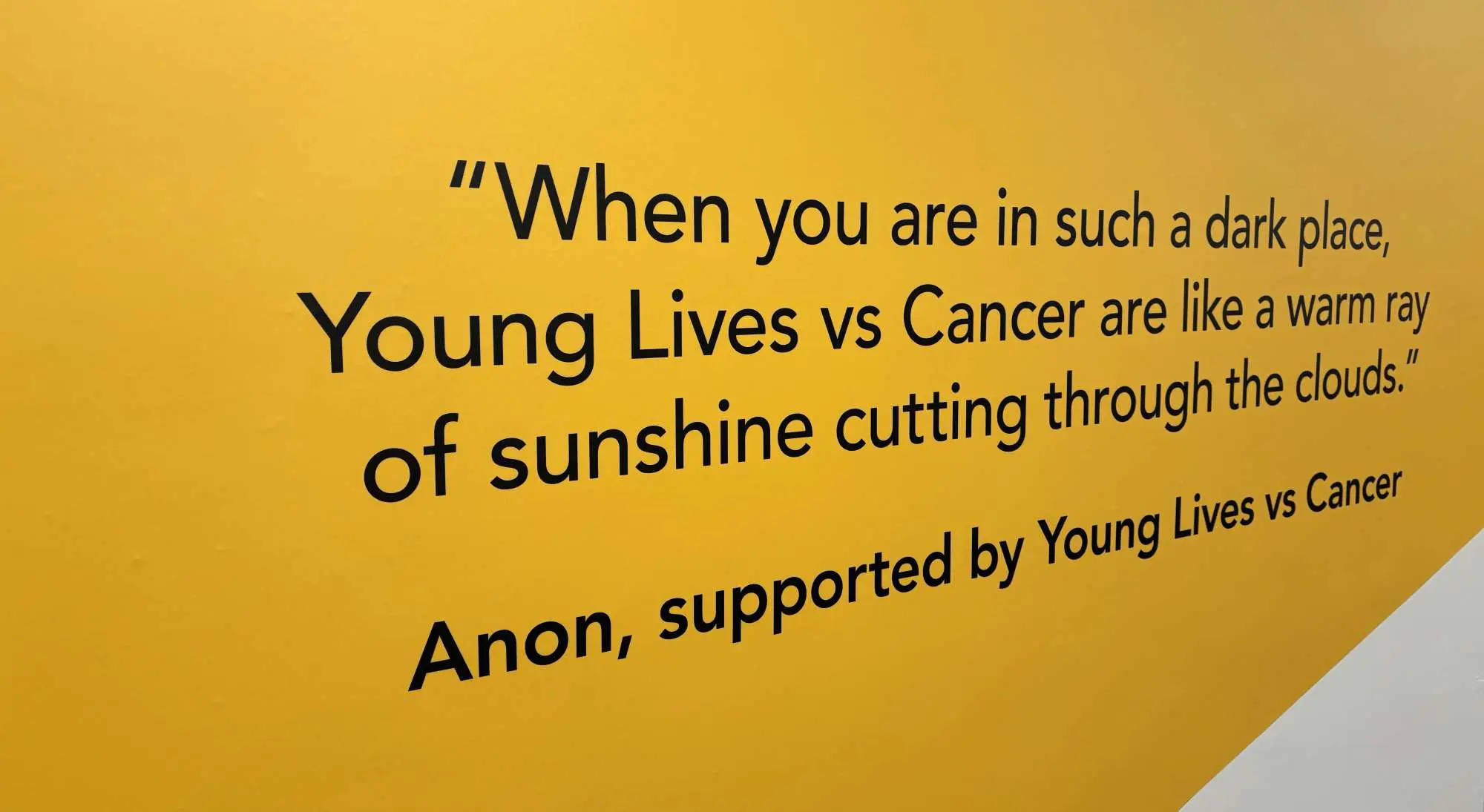 Quote printed on a wall: "When you are in such a dark place, Young Lives vs Cancer are like a warm ray of sunshine cutting through the clouds"