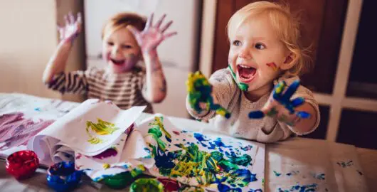 Two happy little girls with dirty hands and faces having fun being creative with finger painting