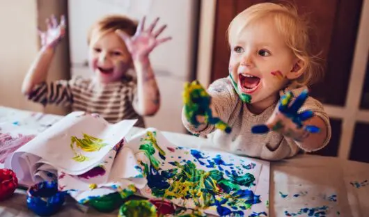 Two happy little girls with dirty hands and faces having fun being creative with finger painting