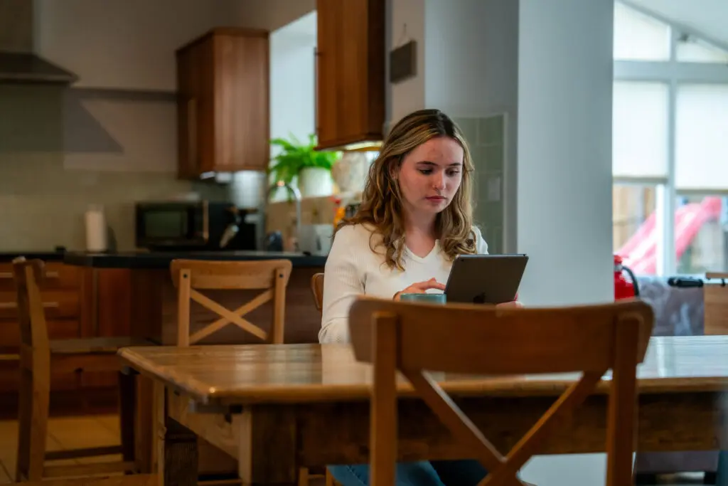 Young person sat at a dining table looking at an ipad.