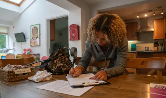 A young person sat at a kitchen table completing paperwork.