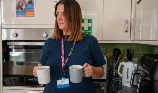 A young Lives vs Cancer Specialist Social worker wearing a branded lanyard standing in a kitchen