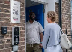 A young person standing on the doorstep of Paul's House, a Young Lives vs Cancer home from home accommodation. Paul's House manager is standing welcoming them through the door.