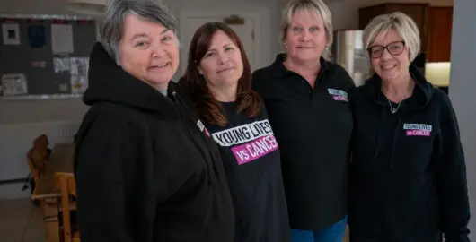 Young Lives vs Cancer accommodation team members in branded hoodies smiling at the camera.