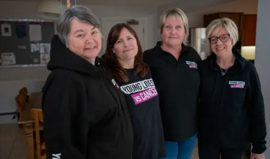 Young Lives vs Cancer accommodation team members in branded hoodies smiling at the camera.