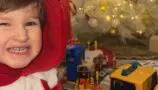 Daithi smiling at the camera wearing a Santa outfit next to a Christmas tree