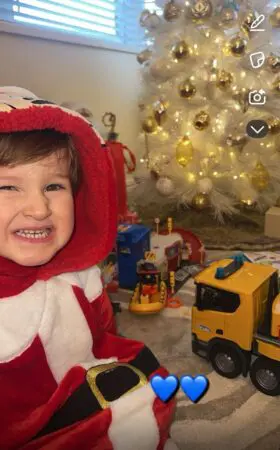 Daithi smiling at the camera wearing a Santa outfit next to a Christmas tree