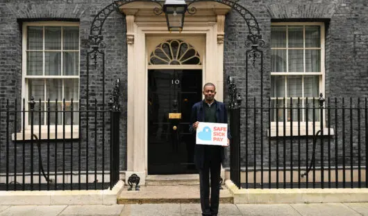 Farid outside 10 Downing Street holding a Safe Sick Pay sign