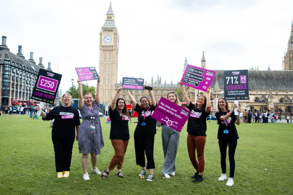 Young Lives vs Cancer campaigners in front of the houses of parliament wearing branded tshirts and holding a banner reading young cancer patient travel fund