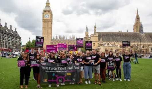 Young Lives vs Cancer campaigners in front of the houses of parliament wearing branded tshirts and holding a banner reading young cancer patient travel fund