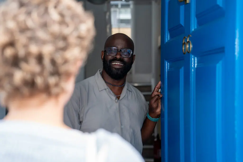 A Young Lives vs Cancer member of staff member opening the door of one of our accommodation services welcoming a young person. 