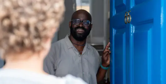 A Young Lives vs Cancer member of staff member opening the door of one of our accommodation services welcoming a young person.