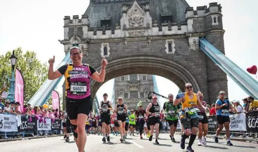 A Young Lives vs Cancer runner at the London Marathon running over Tower Bridge giving a thumbs up to the camera