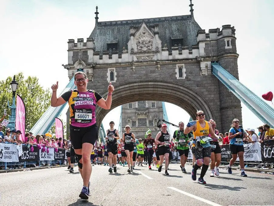 A Young Lives vs Cancer runner at the London Marathon running over Tower Bridge giving a thumbs up to the camera