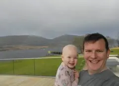 Photo of Indy with her dad, Martin, smiling outside under a rainbow.