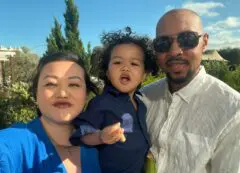 Photo of Kylen with his mum and dad, smiling in the sunshine outside.