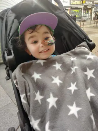 Teddy sitting in a pushchair wearing a cap under a star patterned blanket