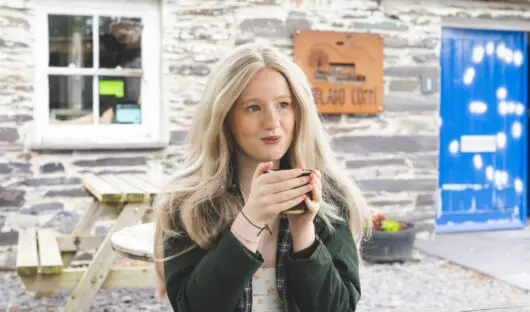 Enlli sat at a picnic bench holding a hot drink.
