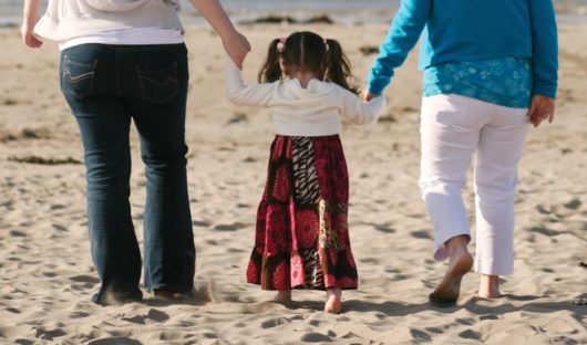 A child with cancer walks on the beach hand in hand with two adults