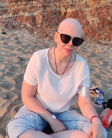 Young cancer patient Vic sitting cross legged on the beach in sunglasses