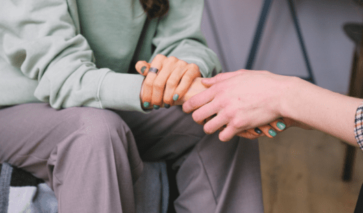 Someone holding another person's hand. One of the people has green painted nails.