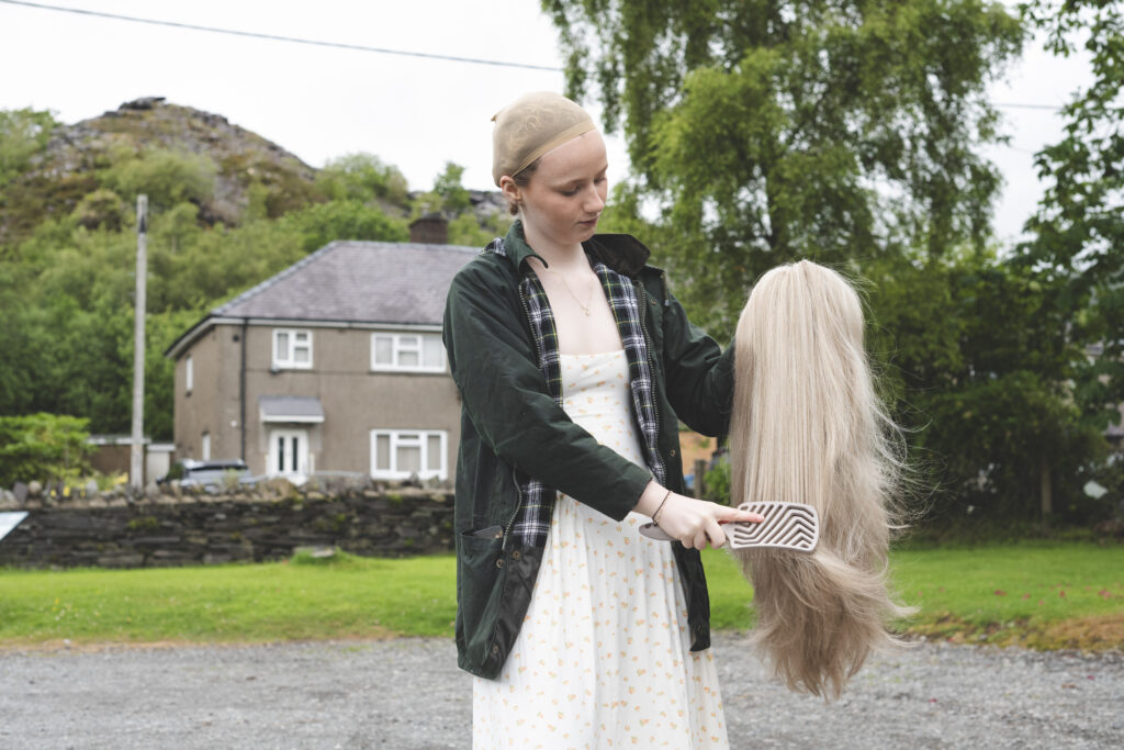 Photo of cancer survivor, Enlli, combing her wig outside of her home in Wales.
