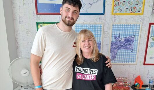 Shon stands next to Rachel with his arm around her, she is wearing a Young Lives vs Cancer t shirt.