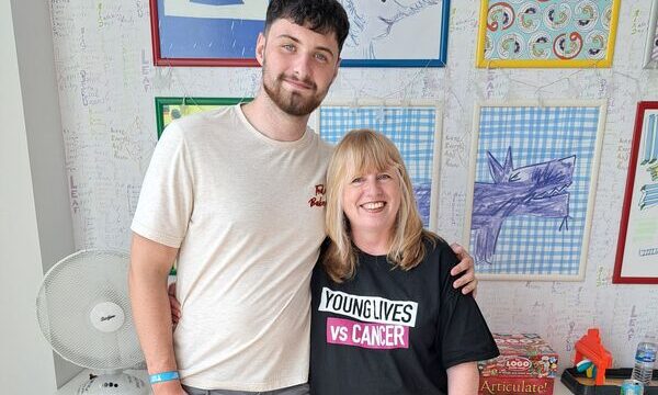 Shon stands next to Rachel with his arm around her, she is wearing a Young Lives vs Cancer t shirt.